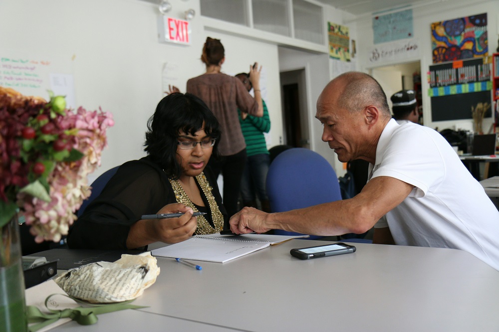  A man and woman collaborate at a table, examining papers and engaging in conversation.